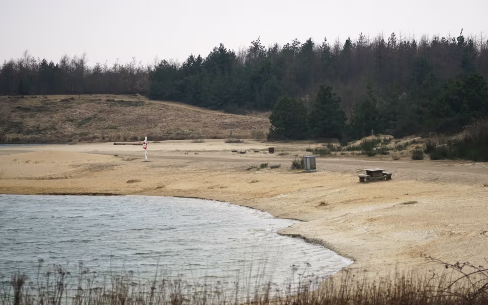 Sandstrand med redningskrans ved Nysø Badesø foran skovklædt skrænt