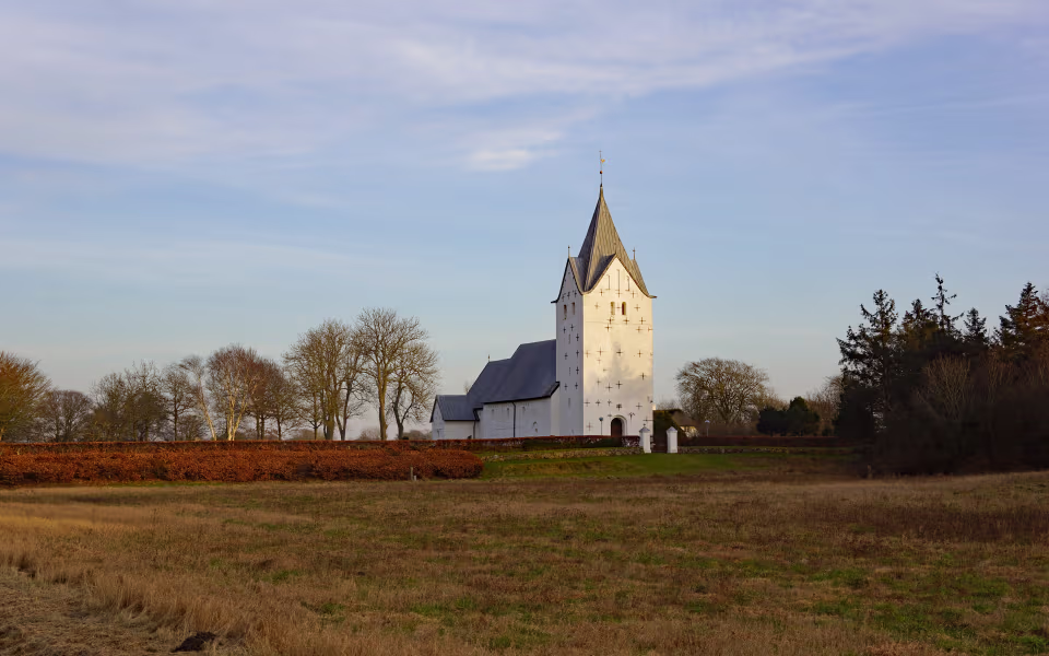 Vester Vedsted Kirke med hvidt tårn bag marker og nøgne træer