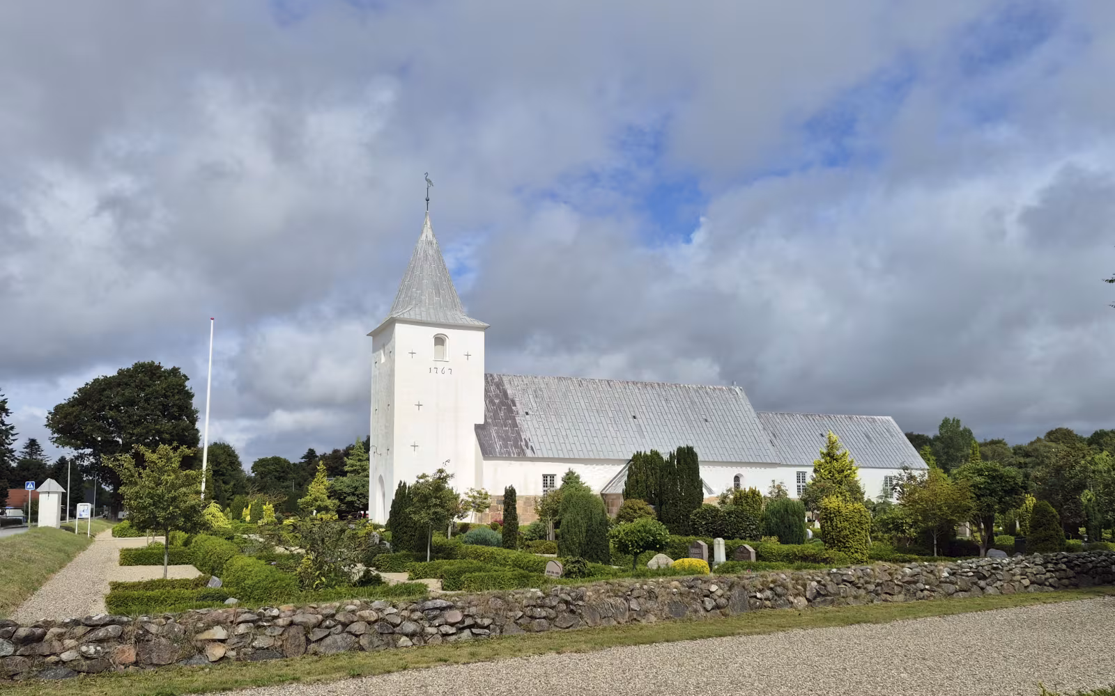 Aal Kirke med hvidt tårn, gråt tag og kirkegård bag lav kampestensmur