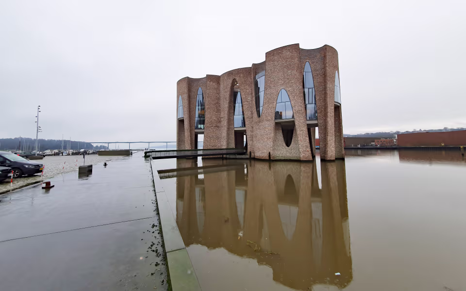 Fjordenhus med buede murstensfacader spejlet i vand ved havnen