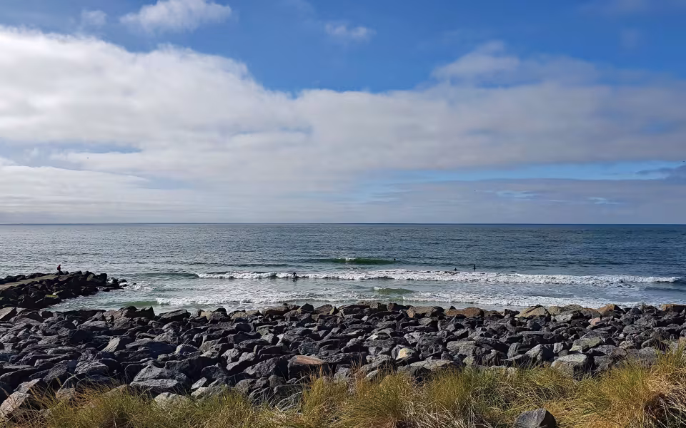 Stenhøfde ved Høfde Q med bølger, surfere og person på klipperne