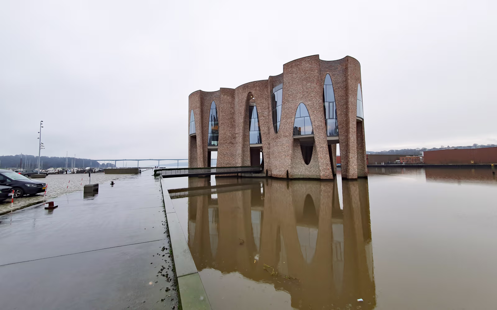 Fjordenhus med buede murstensfacader spejlet i vand ved havnen