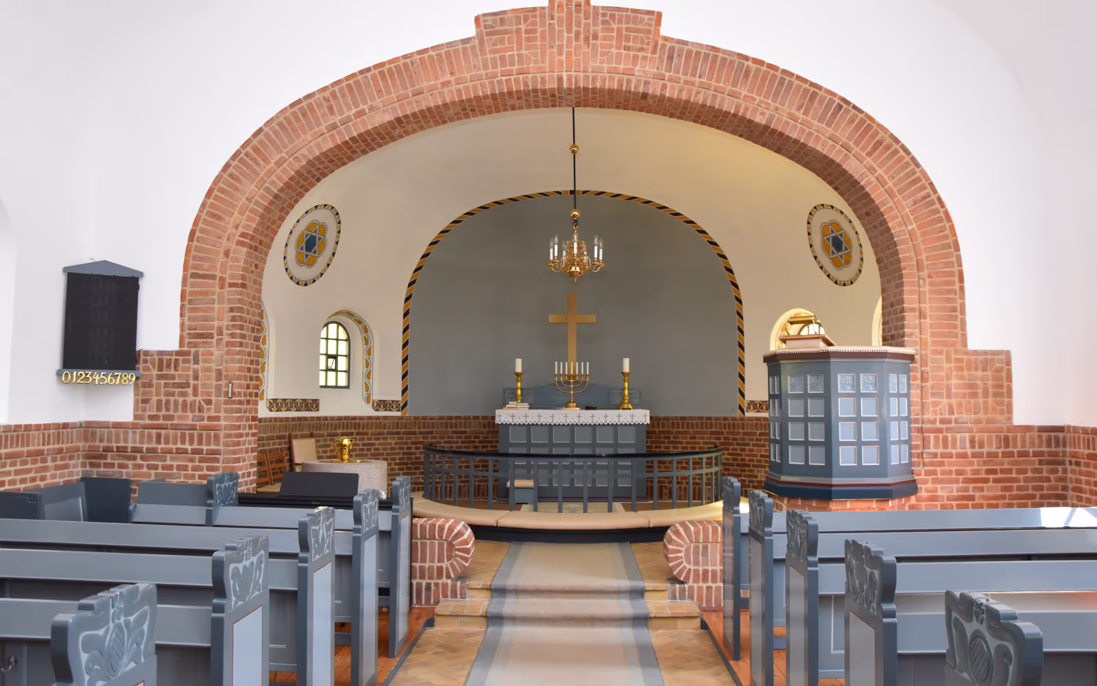 Kirkerum i Urup Kirke med murstensbuer, alter, prædikestol og grå kirkebænke