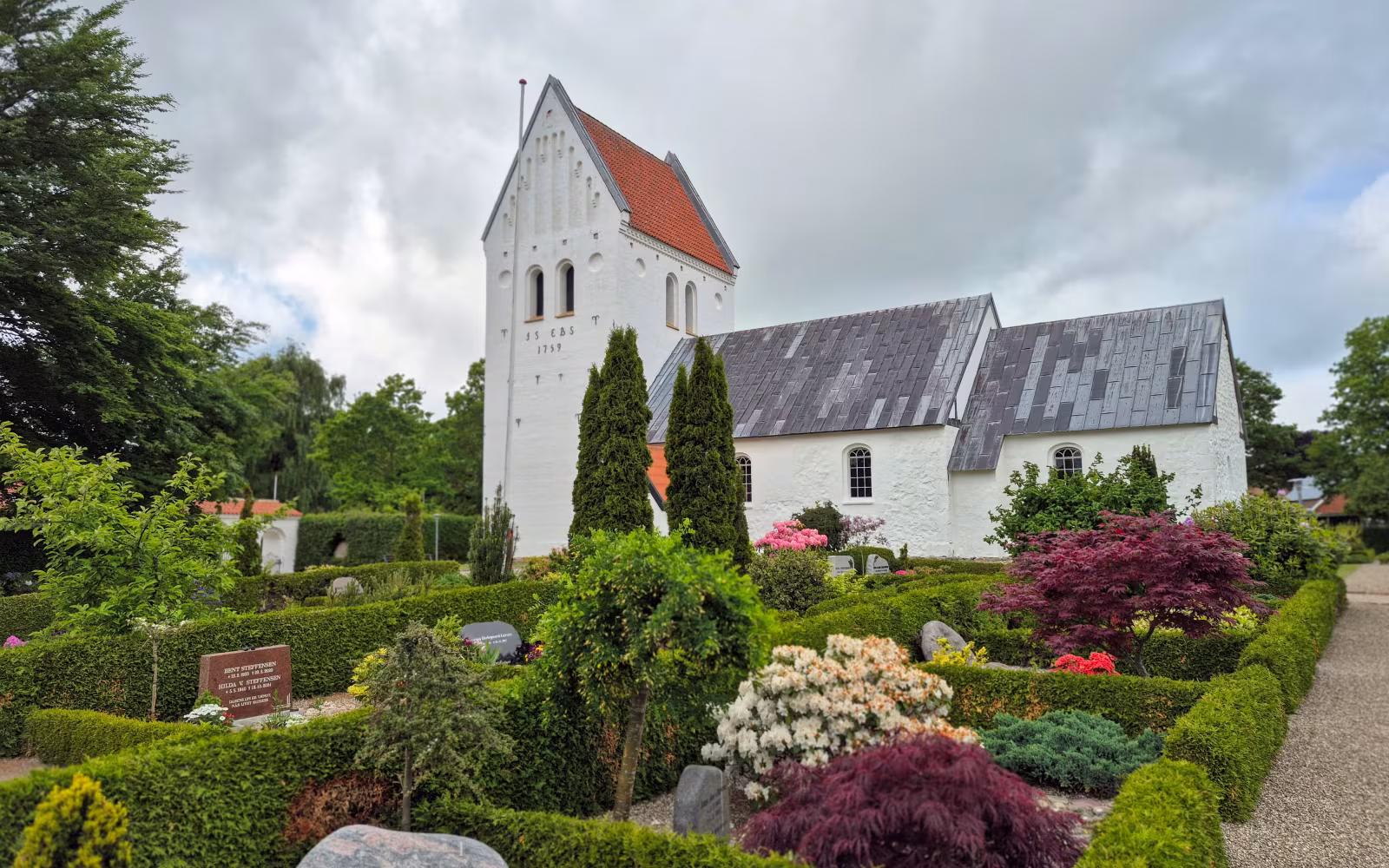 Ryde Kirke med hvidt tårn bag frodig kirkegård med gravsten og hække