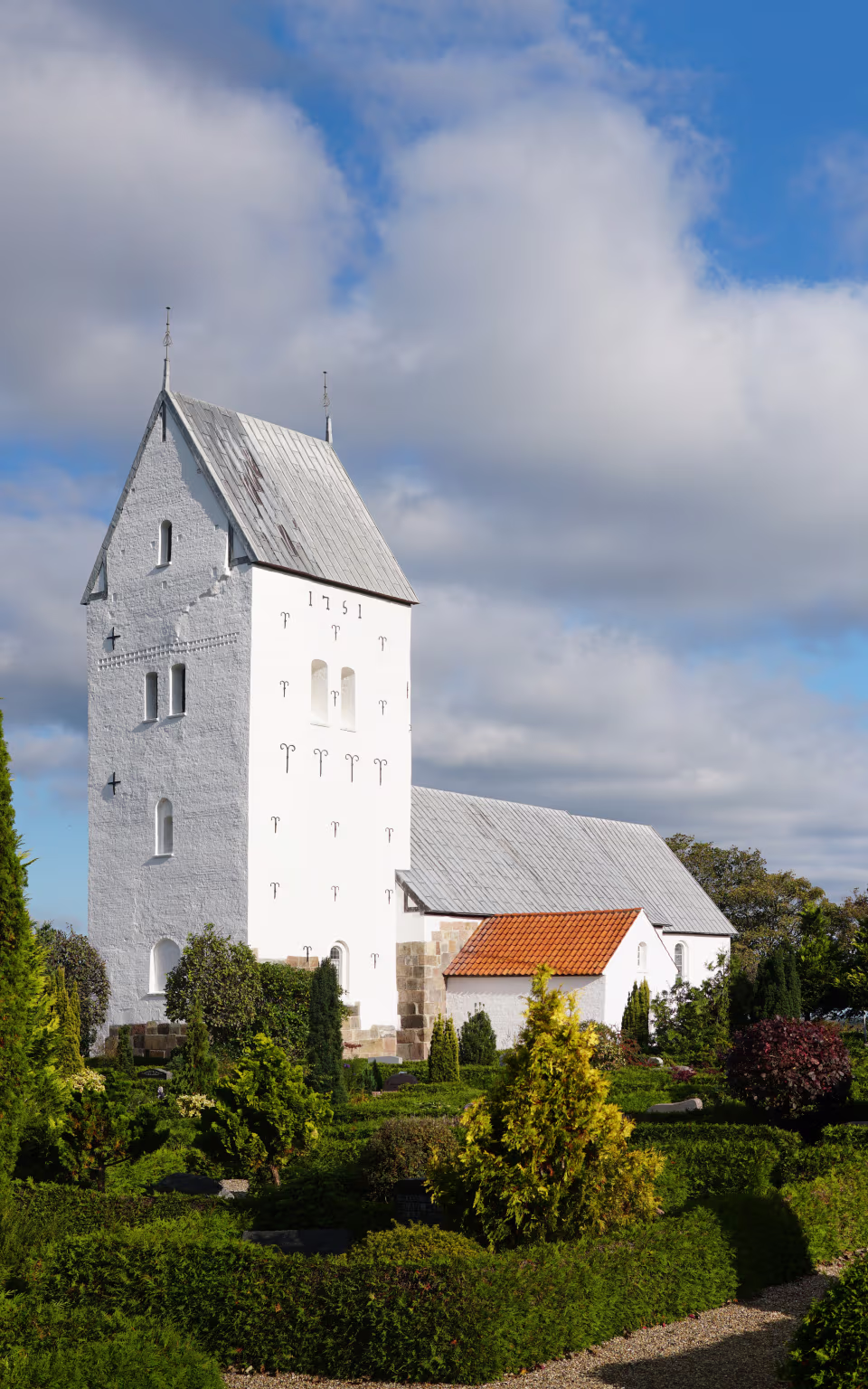 Lønborg Kirke med hvidt tårn bag grøn kirkegård under blå himmel