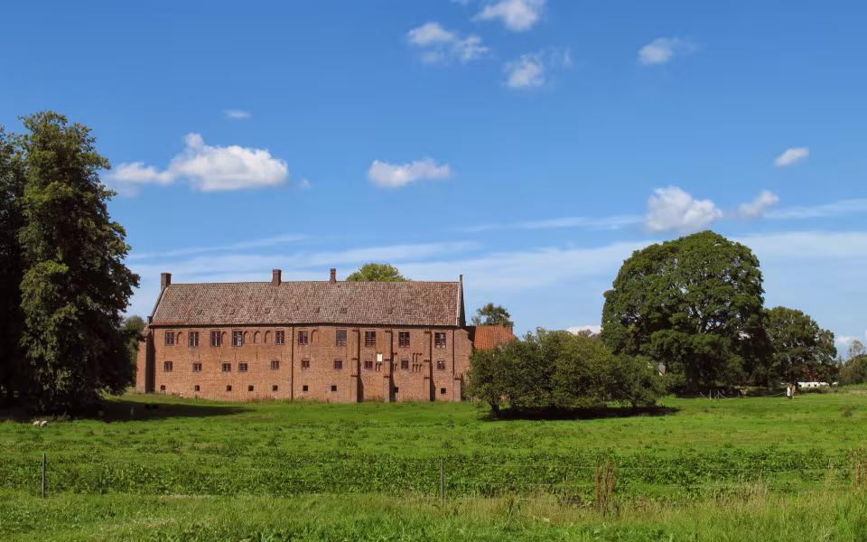 Klosterbygning ved Esrum Kloster bag grøn eng og træer under blå himmel