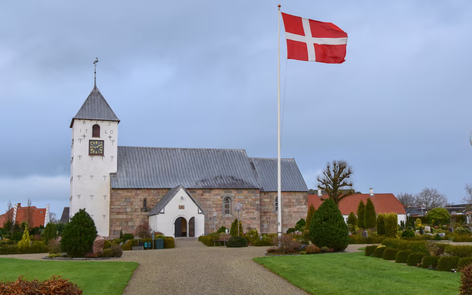 Grussti fører til Horne Kirke med tårn og Dannebrog ved kirkegården