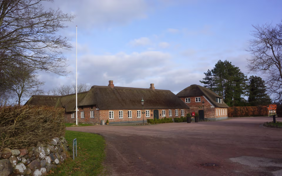 Stråtækt bygning ved Henne Kirkeby Kro med flagstang, gårdsplads og nøgne træer