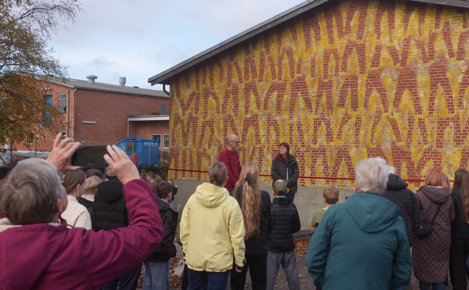 Elever og gæster samles foran slagteriets gavl, hvor gamle jeans er blevet til et farverigt danseværk skabt af Ansager Skole og tekstilkunstner Stine Linnemann.