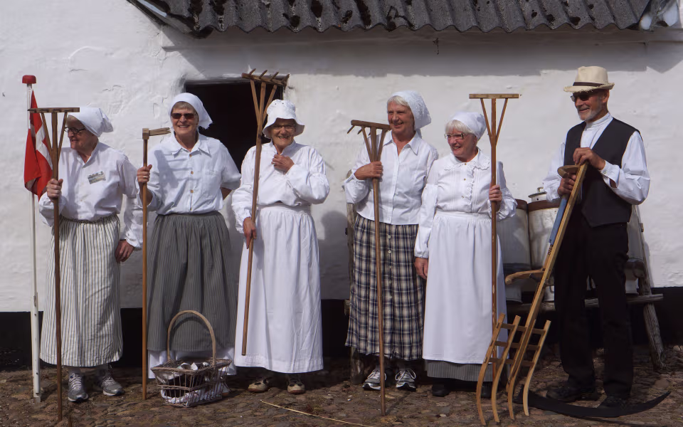 Folk i historiske dragter holder redskaber ved Høstdag på Karensminde
