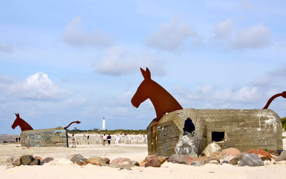 Hesteskulptur på betonbunker ved Blåvand strand med fyrtårn i baggrunden