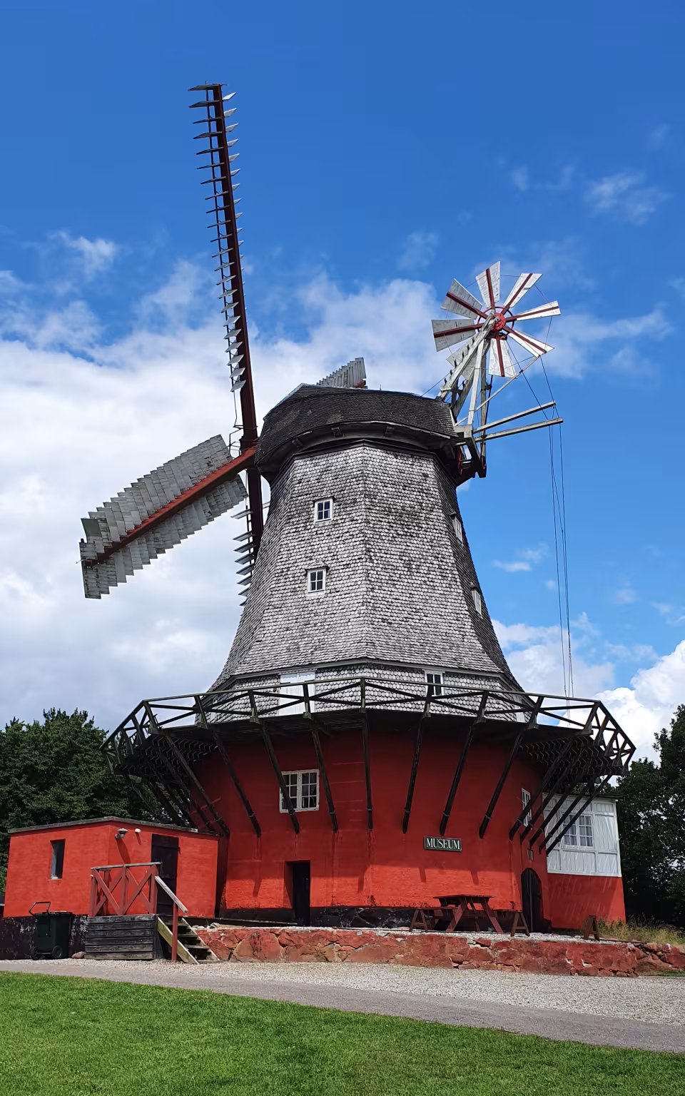 Rød møllebygning med hvide vinger og museums-skilt under blå himmel
