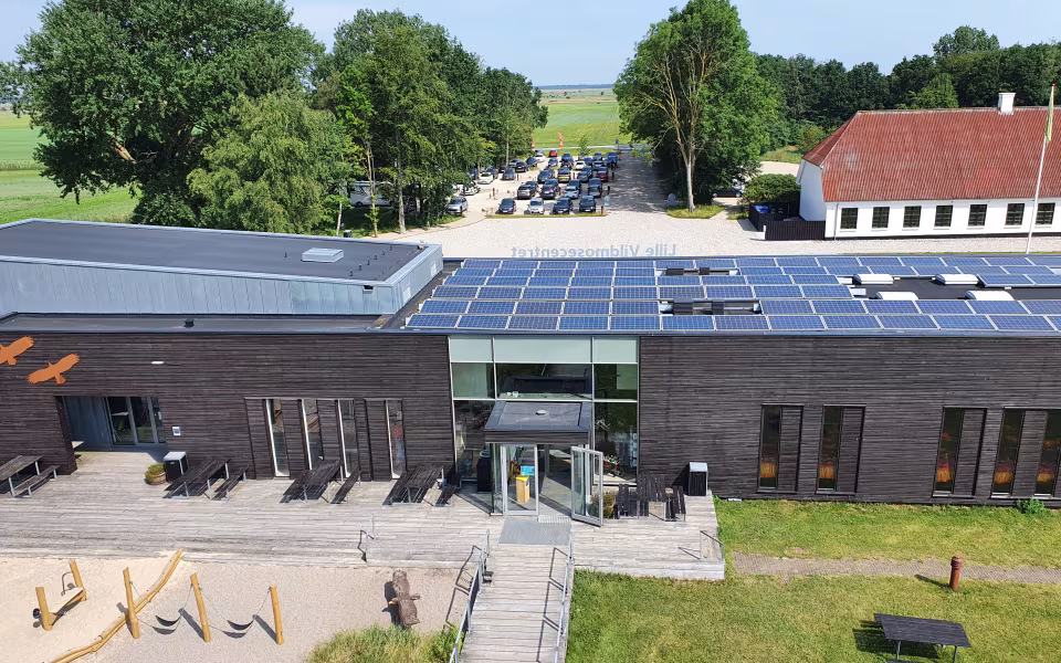 Solcellepaneler på taget af Lille Vildmosecentret med legeplads og skov bagved