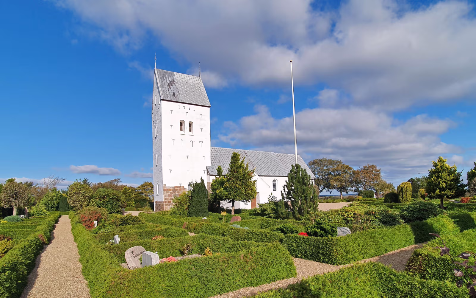 Kirkegårdssti og hvidt kirketårn ved Lønborg Kirke under blå himmel