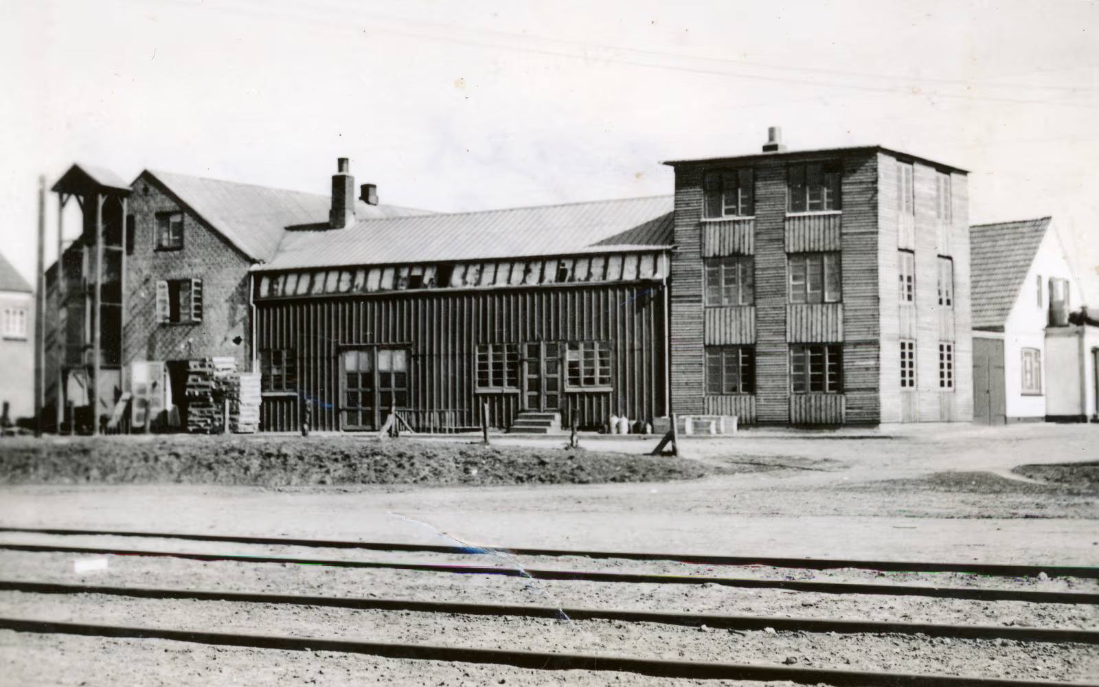 Den gamle møbelfabrik med træfacader, skorstene og skinner i forgrunden