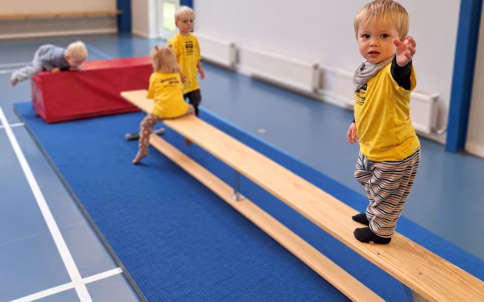Dagplejere og børn mødes til bevægelse i Skovlund-Ansager Hallen, hvor de nye gule trøjer er i brug blandt farverige redskaber.