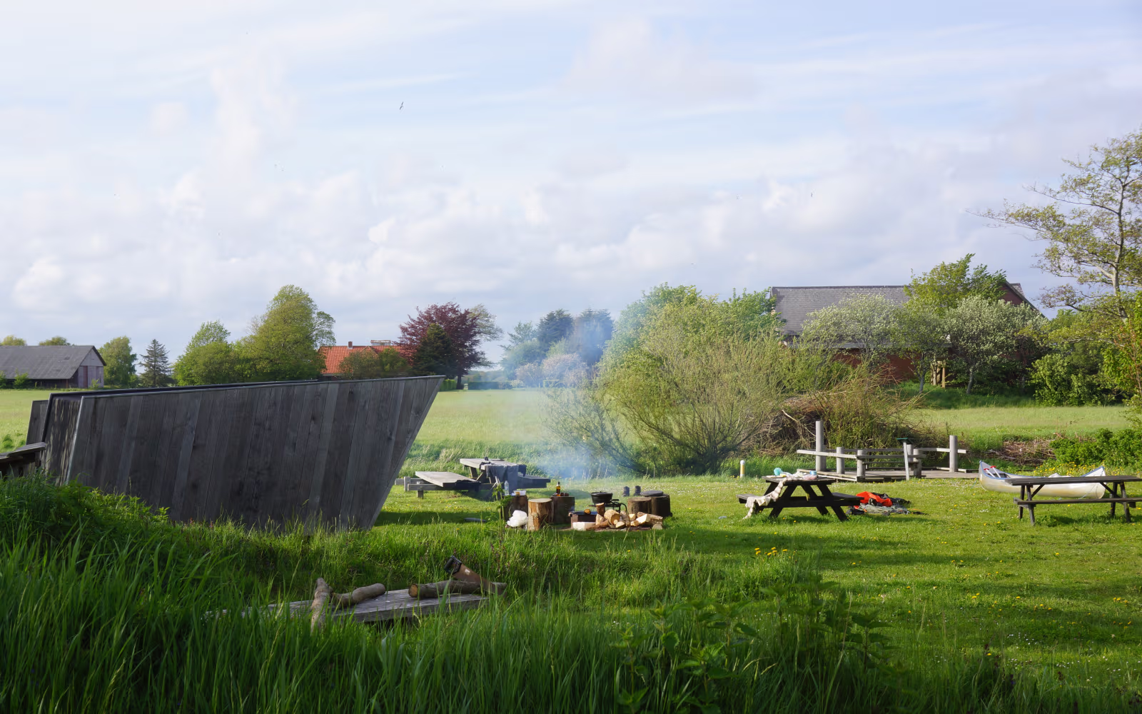 Træshelter ved Kongeåen med picnicborde, kano og røg fra bålplads