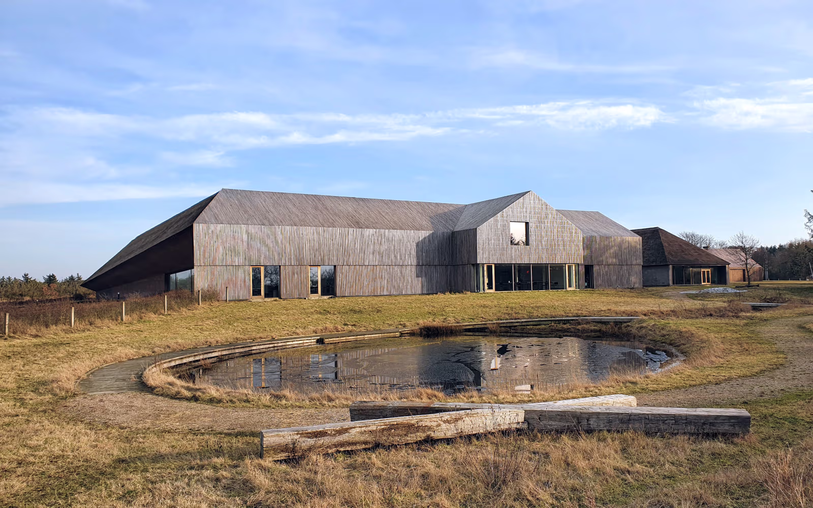 Vadehavscentrets træbygning ved iset vandhul og græsland under blå himmel