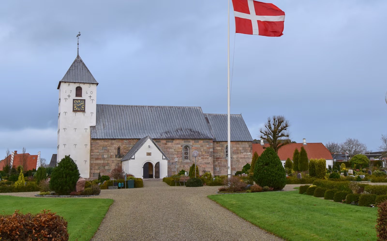 Grussti fører til Horne Kirke med tårn og Dannebrog ved kirkegården