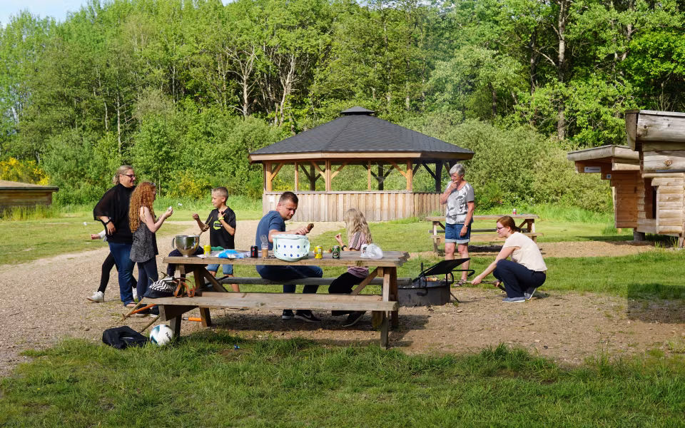 Folk griller og spiser ved picnicborde på Stemmeværkspladsen ved Varde Å