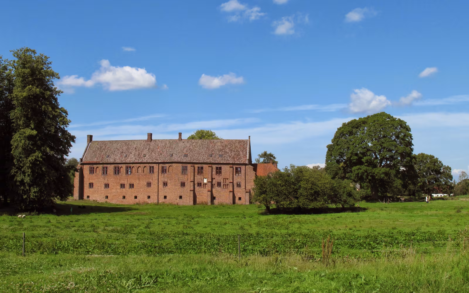 Klosterbygning ved Esrum Kloster bag grøn eng og træer under blå himmel
