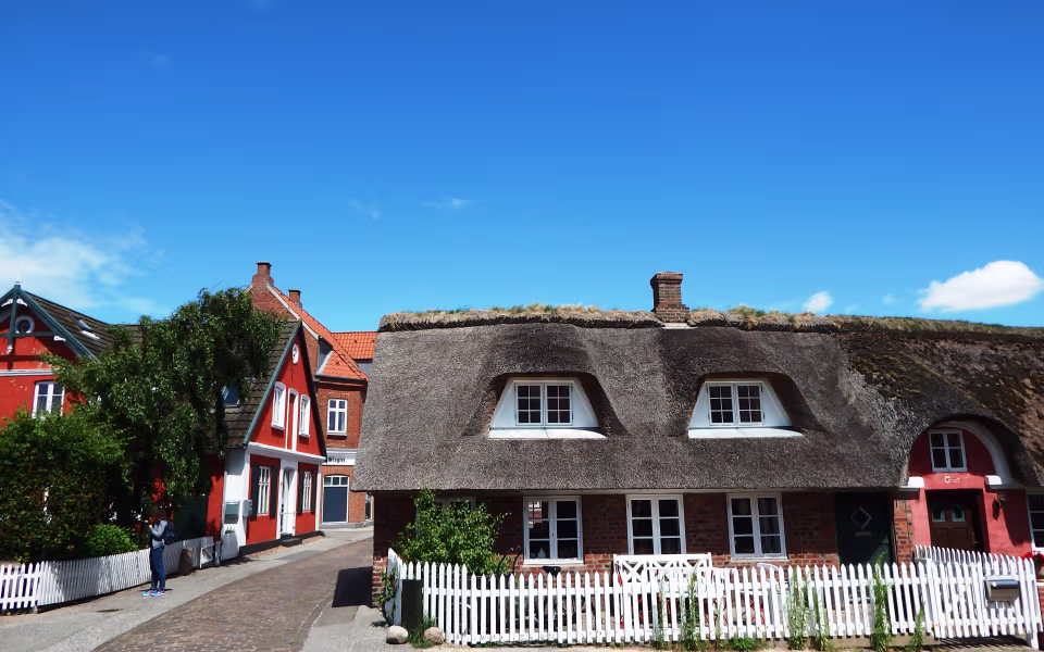 Stråtækte huse og hvide stakitter langs brostensvej på Fanø