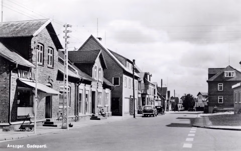 Gadeparti i Ansager med murstenshuse, elmaster og gamle biler langs vejen