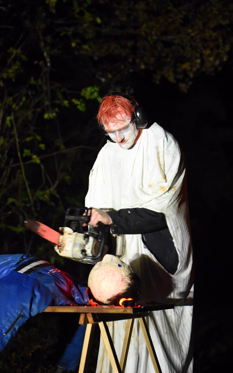 Udklædt person med motorsav ved drive-in halloween i mørk skov
