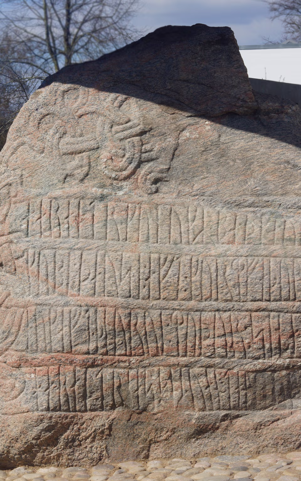 Runesten med indhuggede runer ved Vikingernes Jelling, med besøgende og kirke i baggrunden