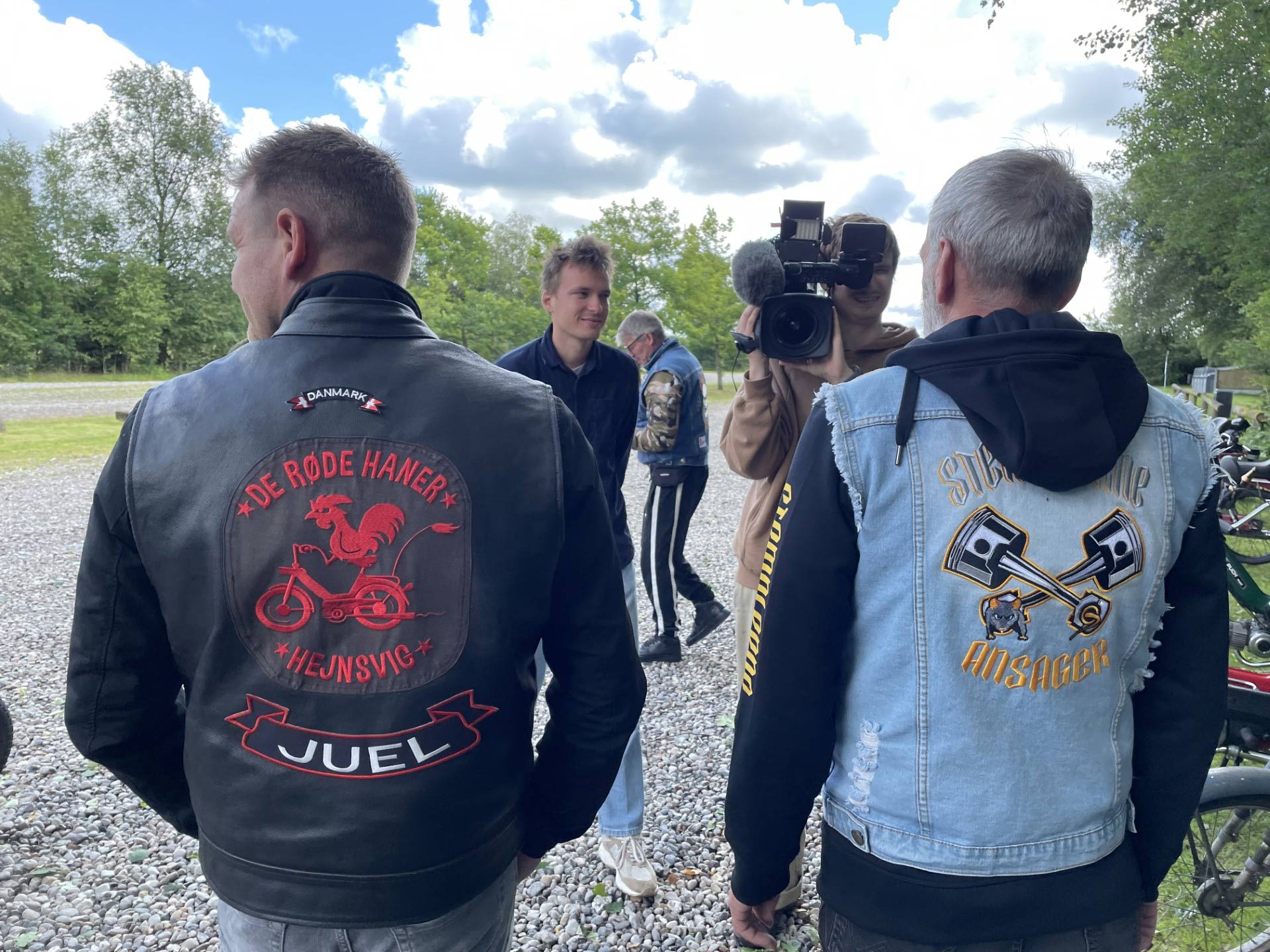 På billedet ses TV2 filme en knallertentusiast fra Stemplerne med klubbens rygmærke. Ved siden af står en medlem fra naboklubben i Hejnsvig med deres eget rygmærke. Fælles passion og fællesskab mellem veteranknallertklubberne vises frem i aftenens nyheder kl. 19:00 på TV2.